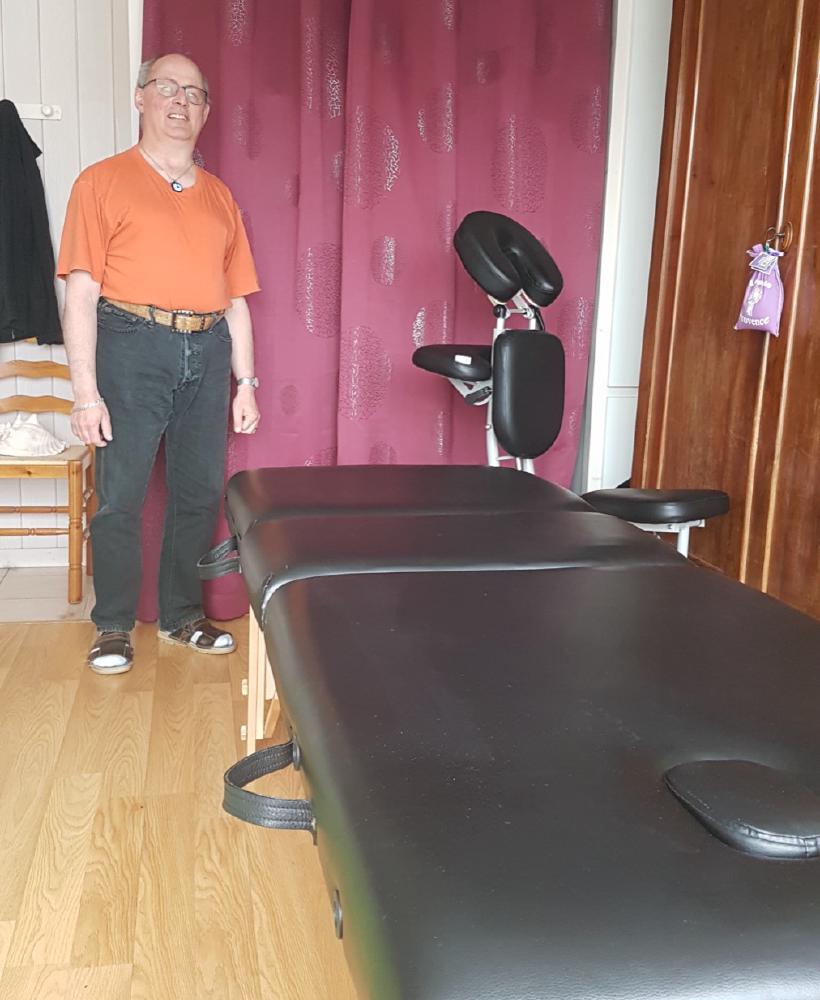 Roger Foucret dans son cabinet de massage, debout près de sa table de massage.